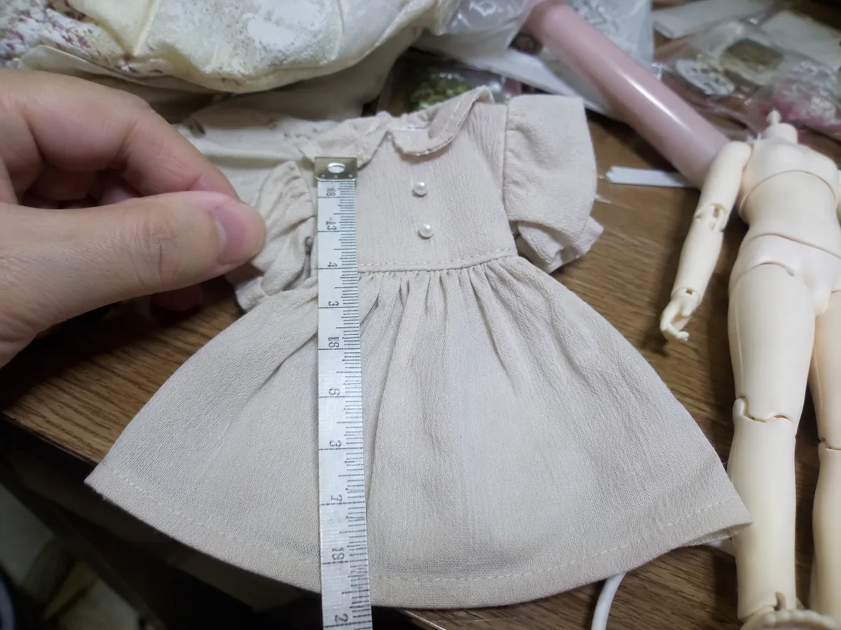Outfit length measured: A buyer measures the dress length beside the doll body, turning fit feedback into a usable sourcing note.